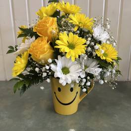 Yellow and white flowers arranged in a smiley-face mug vase