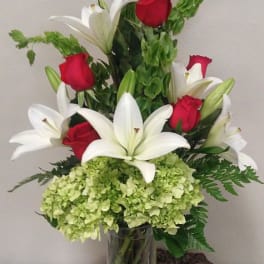 Red roses and white lilies in a glass vase with green hydrangea
