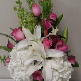 Pink roses and white lilies arranged with white hydrangeas in a glass vase