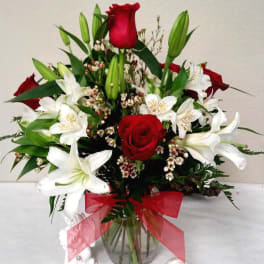 Red roses and white lilies in a glass vase with a pink ribbon