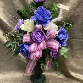 Purple and white floral arrangement in a black vase with a pink ribbon