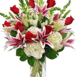 Bouquet of red roses, pink lilies, and white hydrangeas in a glass vase