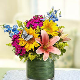 Colorful bouquet with sunflowers, lilies, and blue flowers in a green vase