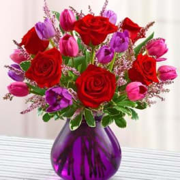 Bouquet of red roses and pink-purple tulips in a purple glass vase