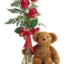 Three red roses in a vase beside a teddy bear