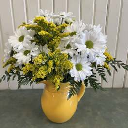 White daisies and yellow filler flowers in a yellow pitcher vase