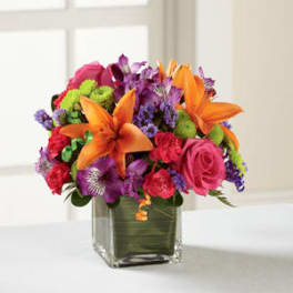 Bright mixed bouquet with orange lilies and pink roses in a square glass vase