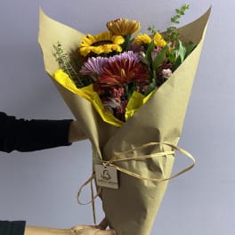 Hand-tied bouquet of mixed colorful flowers wrapped in brown paper