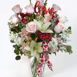 Pink roses and white lilies in a glass vase with a red "love" sign