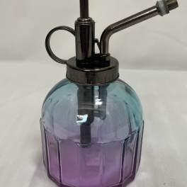 Small blue and purple glass plant mister with dark metal pump and nozzle on a light surface
