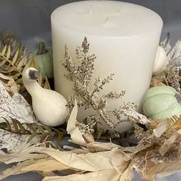 Large white pillar candle surrounded by dried foliage and decorative gourds