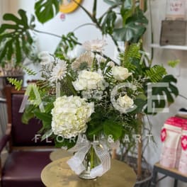 White floral arrangement in a glass vase with a striped ribbon