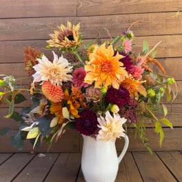Mixed bouquet of dahlias and sunflowers in a white pitcher vase