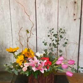 Mixed floral arrangement with sunflowers, lilies, roses, and pink tulips in a rectangular container