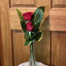 Two red roses in a clear glass vase with assorted greenery