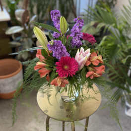 Colorful bouquet with lilies, gerbera daisies, and purple blooms in a glass vase