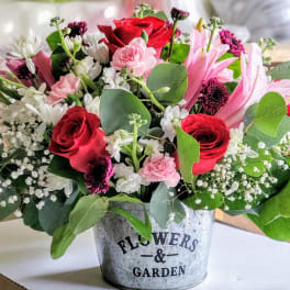 Mixed pink and red flower arrangement in a metal bucket
