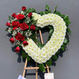 Heart-shaped floral wreath with red roses and white chrysanthemums on an easel
