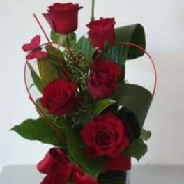 Red roses arranged in a clear glass vase with a red ribbon