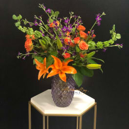 Orange lilies and roses in a purple vase