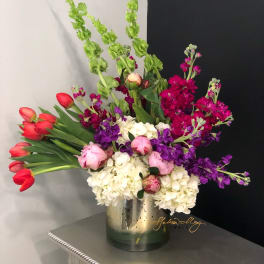Colorful bouquet with red tulips, pink peonies, white hydrangeas, and purple stock in a metal vase