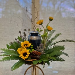 Yellow sunflowers arranged around a dark urn with ferns and branches