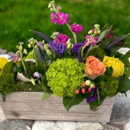 Mixed floral arrangement in a wooden box with bright pink, purple, yellow, and peach blooms