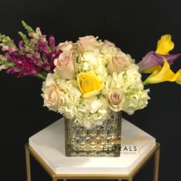 Bouquet of pale roses, white hydrangeas, and yellow calla lilies in a textured vase.