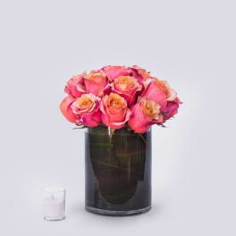 Pink and peach roses arranged in a dark glass vase beside a small candle.