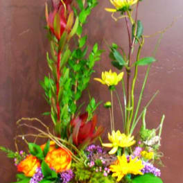 Tall mixed floral arrangement with yellow and orange blooms in a low container
