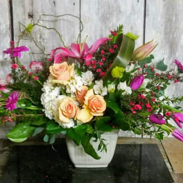 Mixed floral arrangement in a white square vase with pink lilies and roses