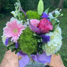 Pink and white floral bouquet in a glass vase with a purple ribbon