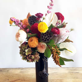 Mixed bouquet with white anthuriums, roses, and bright blooms in a dark vase