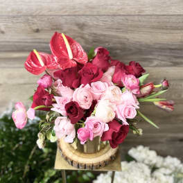 Pink and red roses with red anthuriums arranged in a wooden container