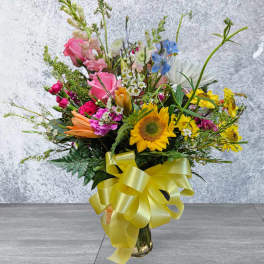 Mixed bouquet with sunflowers, pink roses, and a yellow ribbon in a glass vase