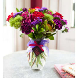 Bouquet of red, purple, and pink flowers in a glass vase with a ribbon