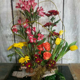 Mixed floral arrangement with pink, yellow, orange, and red blooms in a low base