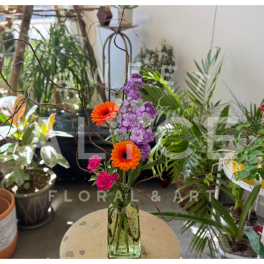 Orange and pink flowers in a green glass vase with curly branches