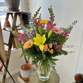 Mixed bouquet with yellow lilies, pink gerberas, and orange roses in a clear vase