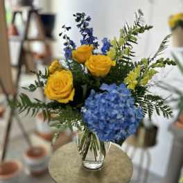 Bouquet of yellow roses and blue hydrangeas in a clear glass vase