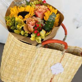 Bouquet of sunflowers, peach roses, and yellow flowers in brown paper