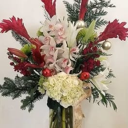 Tall holiday bouquet with white orchids, red accents, and evergreen branches in a glass vase