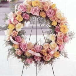 Pastel wreath of pink, peach, and yellow roses displayed on a metal easel stand