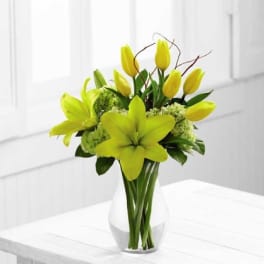Vase of bright yellow lilies, tulips, and green hydrangeas on a white table