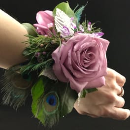 Pink rose wrist corsage with peacock feathers and greenery