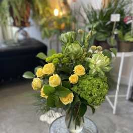 Yellow roses and green flowers in a clear glass vase