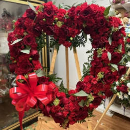 Heart-shaped red rose wreath on a wooden stand with a red ribbon