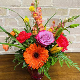 Bright mixed bouquet in a purple glass vase with orange, pink, and red blooms