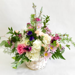 Mixed bouquet of pink, white, and purple flowers in a white basket