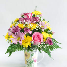 Mixed bouquet in a floral mug vase with pink, yellow, and purple blooms